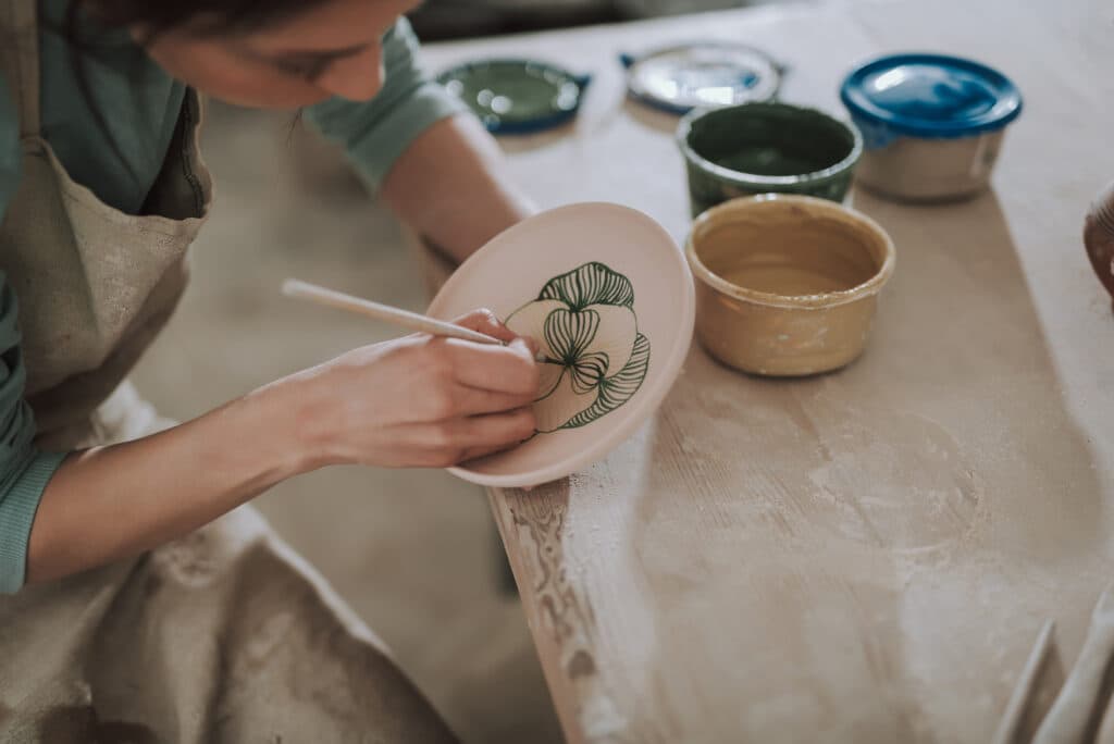 Young lady in apron painting ceramic plate at workshop