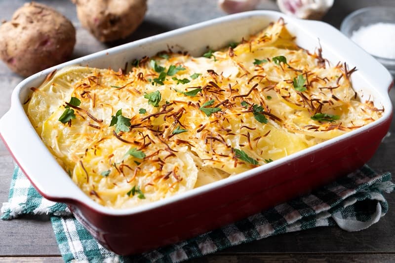 Potato gratin baked with cream and cheese on wooden table.