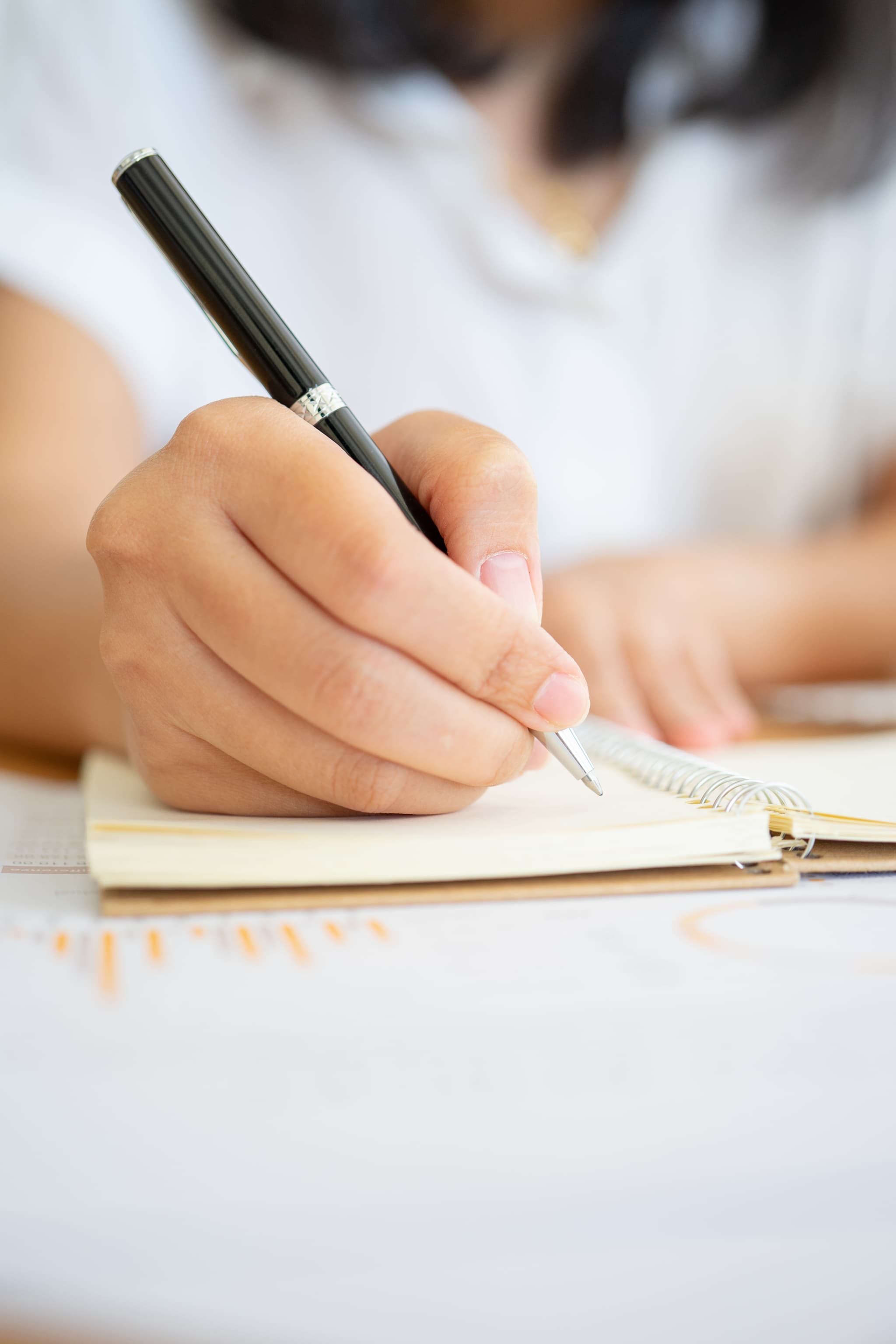 Close shot of businesswoman hands holding a pen writing something on the paper on the foreground in office. Recording concept